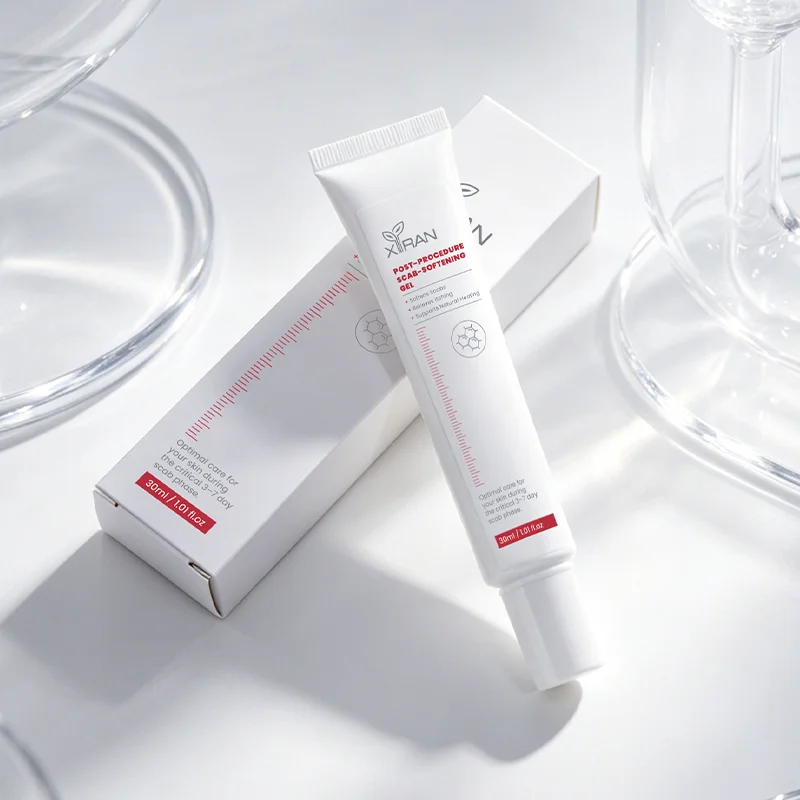 A white tube of scar-softening gel with its box on a reflective surface, surrounded by glass objects, featuring a minimalist design.